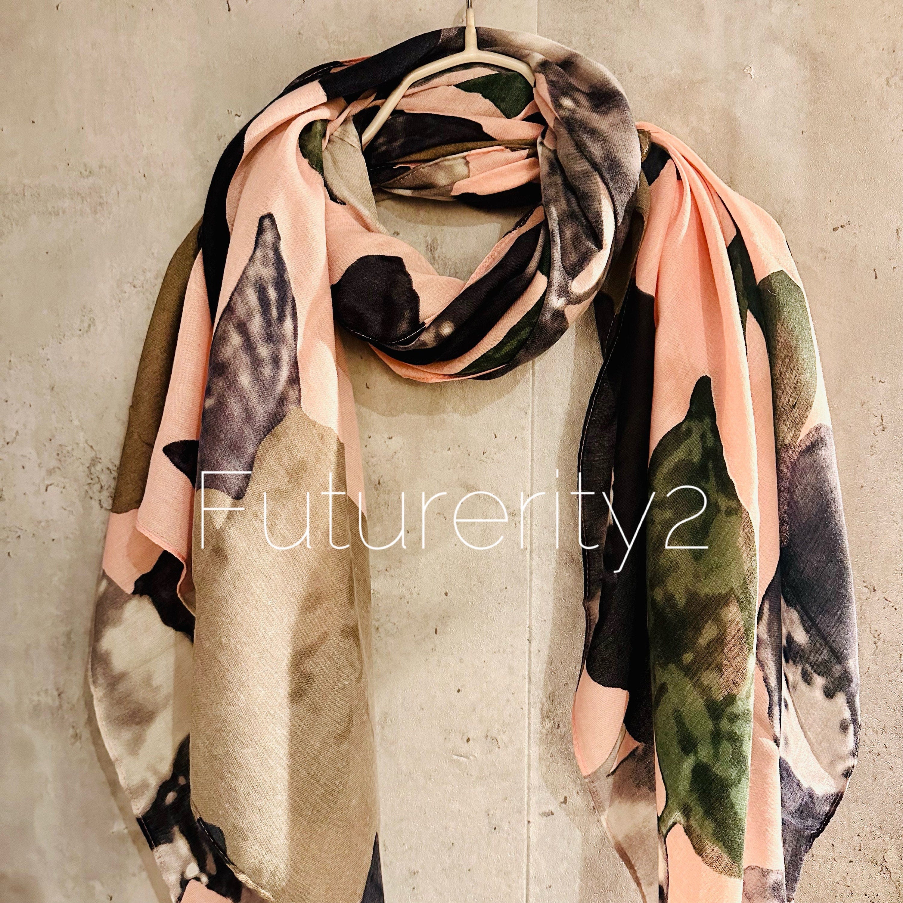 A pink and black patterned scarf with a floral design. The scarf is made of a soft, lightweight fabric and has a fringed edge.