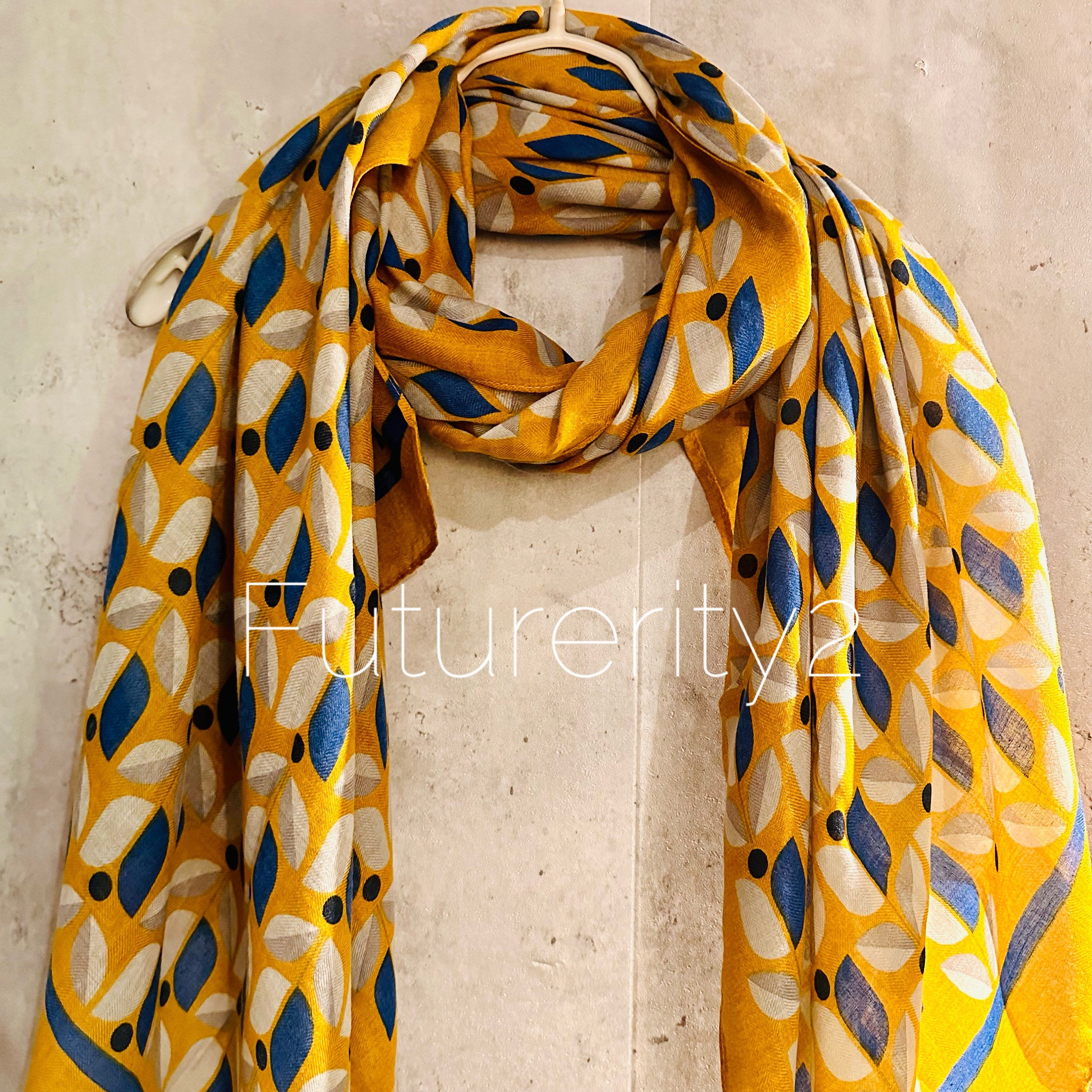 A mustard yellow and blue patterned scarf with a floral design. The scarf is made of a soft, lightweight fabric and has a fringed edge.